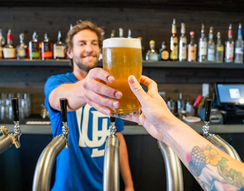 Friendly bartender handing a pint in a lively pub setting.