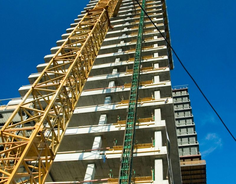Low-angle view of skyscraper under construction with crane, clear blue sky.